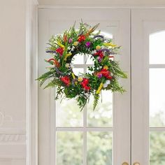 a wreath hanging on the front door of a house with flowers and greenery in it