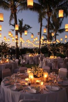 an outdoor dinner setting with paper lanterns hanging from the ceiling and candles lit up in the air