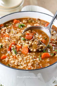 a spoon full of soup with carrots, barley and parsley on the side