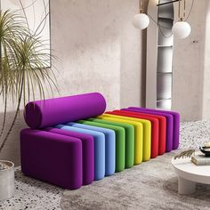 a rainbow colored couch sitting on top of a white floor next to a potted plant