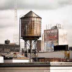 an old rusted water tower on top of a building with other buildings in the background