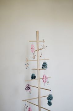 an art piece made out of wood sticks and pine cones with ornaments hanging from them