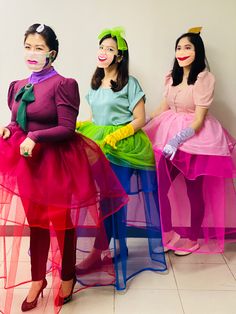 three women in colorful dresses and masks sitting next to each other