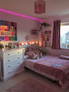 a bedroom with pink walls and lots of pictures on the wall above the bed is lit up by colorful lights