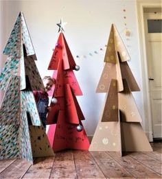 three cardboard christmas trees are on the floor in front of a wall with writing on them