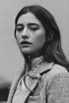 a woman with long hair wearing a coat and looking off to the side in black and white