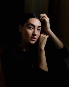 a woman is sitting in the dark with her hand on her head and looking off into the distance