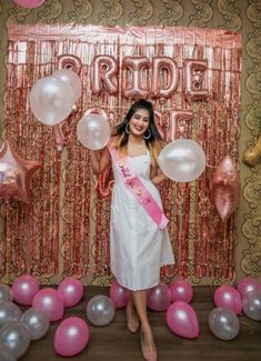 a woman standing in front of balloons and streamers with a sash around her waist