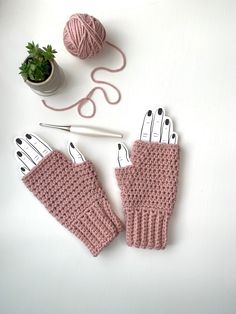 knitted gloves and knitting needles on top of a white table with a potted plant