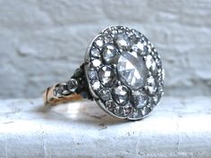 an antique diamond ring is sitting on a stone surface in front of a white brick wall