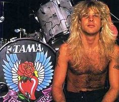 a shirtless man with long hair sitting in front of a drum kit on stage