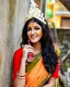 a woman in an orange and green sari with a crown on her head posing for the camera