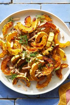 a white plate topped with roasted squash and onions on top of a blue tile floor