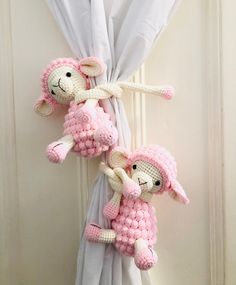 two crocheted stuffed animals hanging from a curtain with white curtains in the background