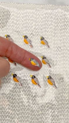 a person's finger pointing at some tiny yellow and black birds on white paper