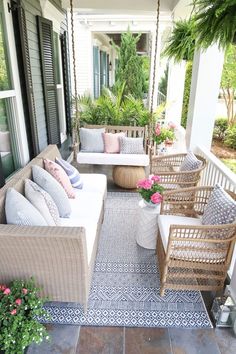 the porch is decorated with white wicker furniture and pink flowers in vases on hanging chairs