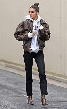 a woman walking down the street wearing black pants and a brown jacket with hoodie on