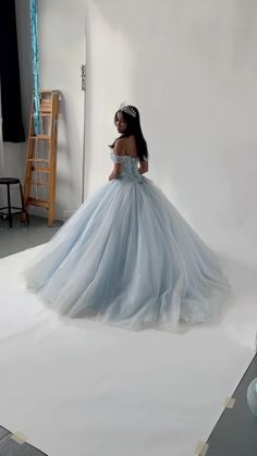 a woman in a blue dress is standing on a white floor and wearing a tiara