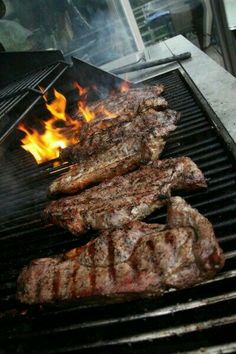 two steaks cooking on the grill with flames coming out of it's sides