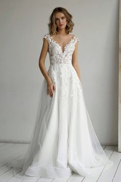 a woman in a white wedding dress standing on a wooden floor next to a wall