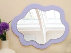 a purple mirror sitting on top of a table next to a vase with flowers in it