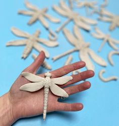 a person's hand holding a dragonfly ornament on a blue background