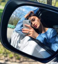 a woman looking at her cell phone in the side view mirror