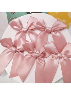 three pink bows are on top of a white plate with a book in the background