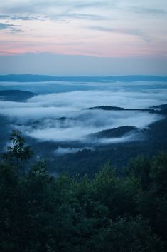 the sky is filled with low lying clouds in the distance, as seen from an overlook