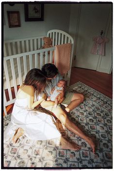 a man and woman holding a baby in their lap on the floor next to a crib