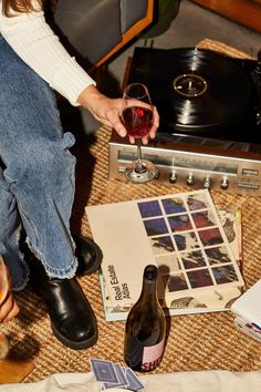 a person sitting on the floor holding a glass of wine next to record players and records