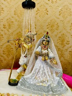 two figurines dressed in white and gold are standing next to each other on a table