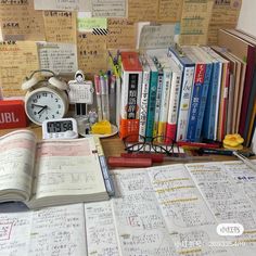 an open book sitting on top of a desk next to a clock and many books