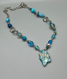 This multi-fashion stone pendant necklace will get you noticed with its sky blue color and unique center stone. Wear it year-round with everything from casual and weekend wear to more sophisticated ensembles with confidence. Handmade using a variety of mediums, this one-of-a-kind choker necklace will set the stage for any outfit you put on.  #handmadejaspernecklace #doubleddezinez #blueskybeadedchoker #uniquedesignjewelry #mixedmediumnecklace #unisexchoker #bohoinspiredjewelry Blue Chrysocolla Necklace With Stones, Blue Gemstone Beads Necklace In Mineral Crystal, Handmade Blue Mineral Crystal Necklace, Handmade Blue Chrysocolla Beaded Necklaces, Handmade Turquoise Blue Agate Necklace, Unique Blue Beaded Necklaces With Stones, Handmade Blue Turquoise Agate Necklace, Handmade Blue Agate Turquoise Necklace, Blue Turquoise Necklace With Wire Wrapped Round Beads