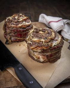 two pastries sitting on top of a cutting board next to a knife and napkin