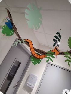 an orange and black snake on a branch in the middle of a room with white walls