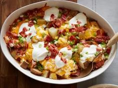 a white bowl filled with potatoes, bacon and sour cream on top of a wooden table