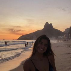 a woman standing on top of a sandy beach next to the ocean at sun set