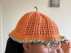 a woman wearing an orange crocheted hat with green trim on her head and glasses