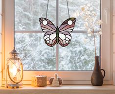 a stained glass butterfly hanging from a window sill next to a vase and candle