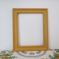 an empty wooden frame sitting on top of a floral table cloth next to a white wall