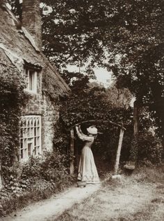 an old photo of a woman standing in front of a house