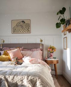 a bed with pink and gold pillows in a bedroom next to a painting on the wall