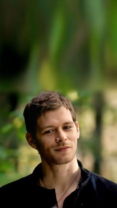 a man in black shirt looking at the camera with blurry trees in the background