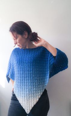 a woman wearing a blue and white crochet sweater standing in front of a wall