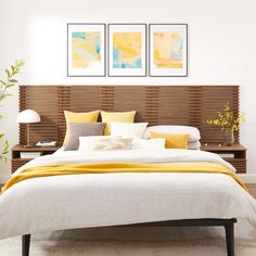 a bed with yellow and white pillows in a room next to two pictures on the wall