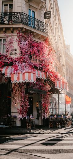 the outside of a restaurant with pink flowers growing on it's windows and awnings