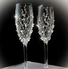 two wine glasses with white flowers and leaves on the bottom one is clear, while the other is crystal