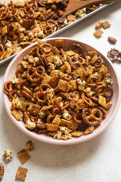 a pink bowl filled with cheerios next to a tray of pretzels and crackers