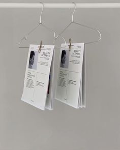 two papers hanging from clothes pins on a metal hanger in front of a gray wall